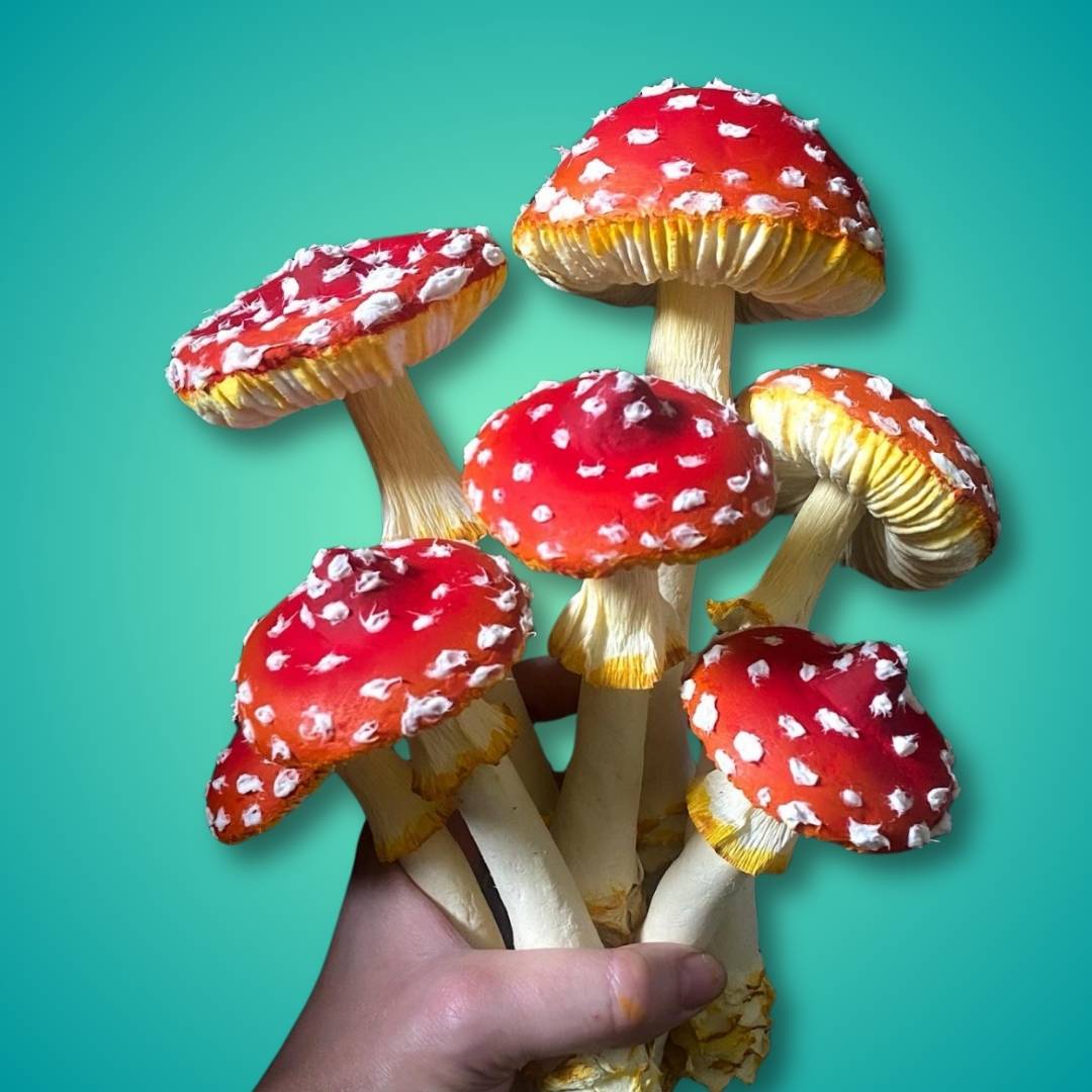 Papier-mâché amanita mushrooms with red caps and white spots – handmade craft held in hand on teal background