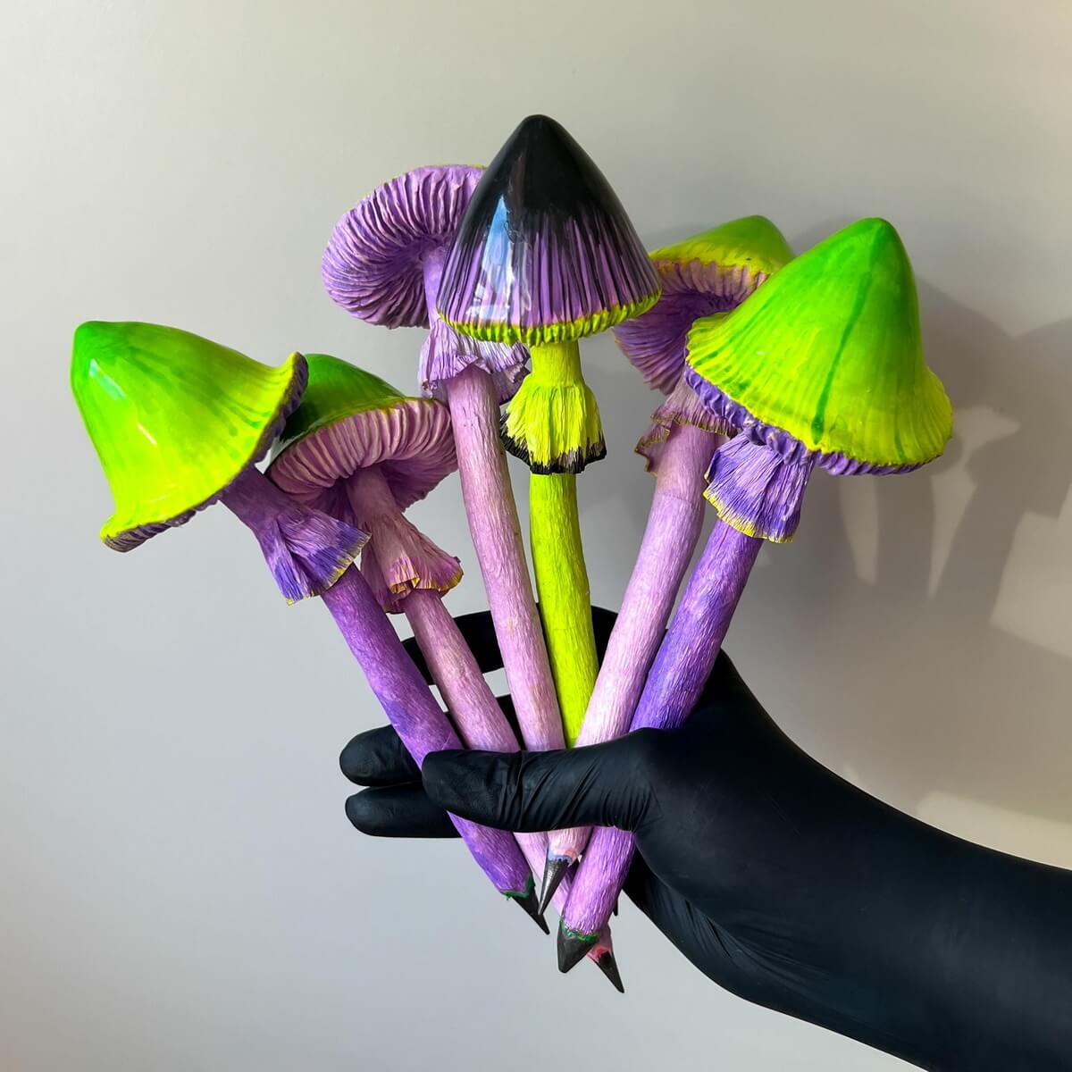 Purple and green papier-mâché mushroom pencil in motion – quirky sculpture on black background