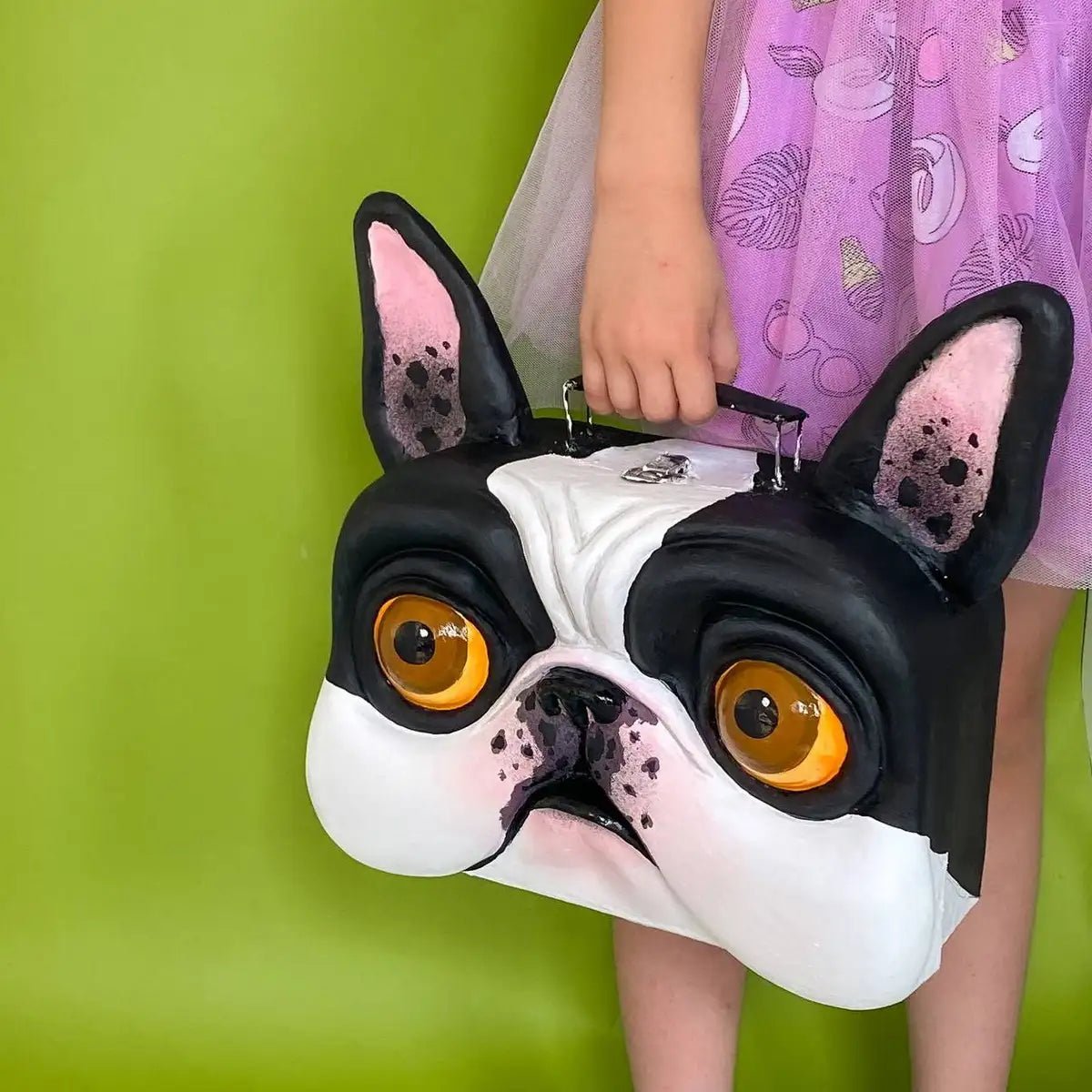 Decorative bulldog suitcase shown held in hand against green background