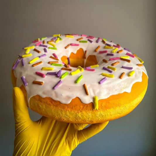 Handmade white donut with colorful sprinkles held in yellow gloves