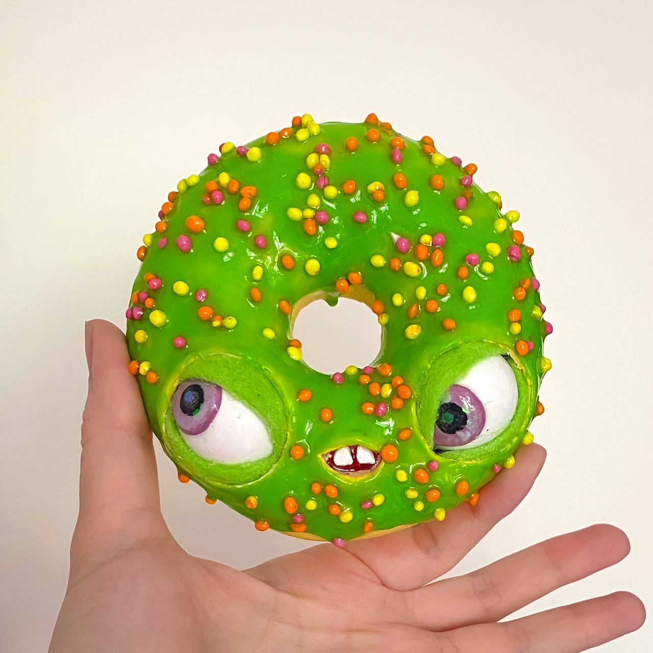 Green papier-mâché donut with colorful candy topping and goofy face – handmade craft held in hand