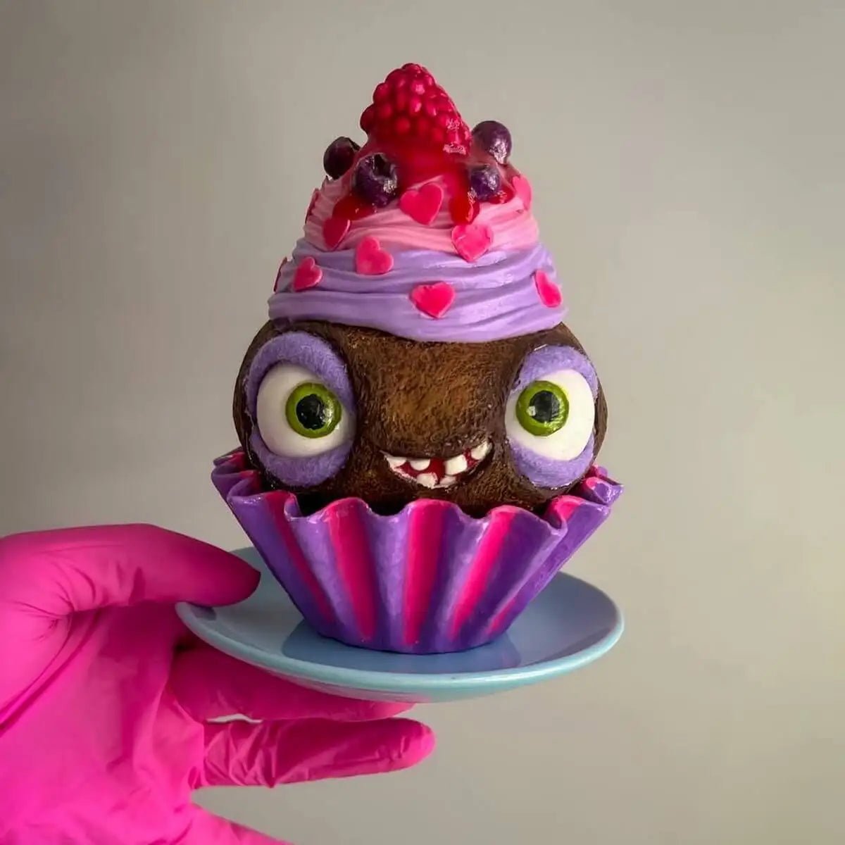 Cupcake with raspberry top standing on a blue saucer – front view