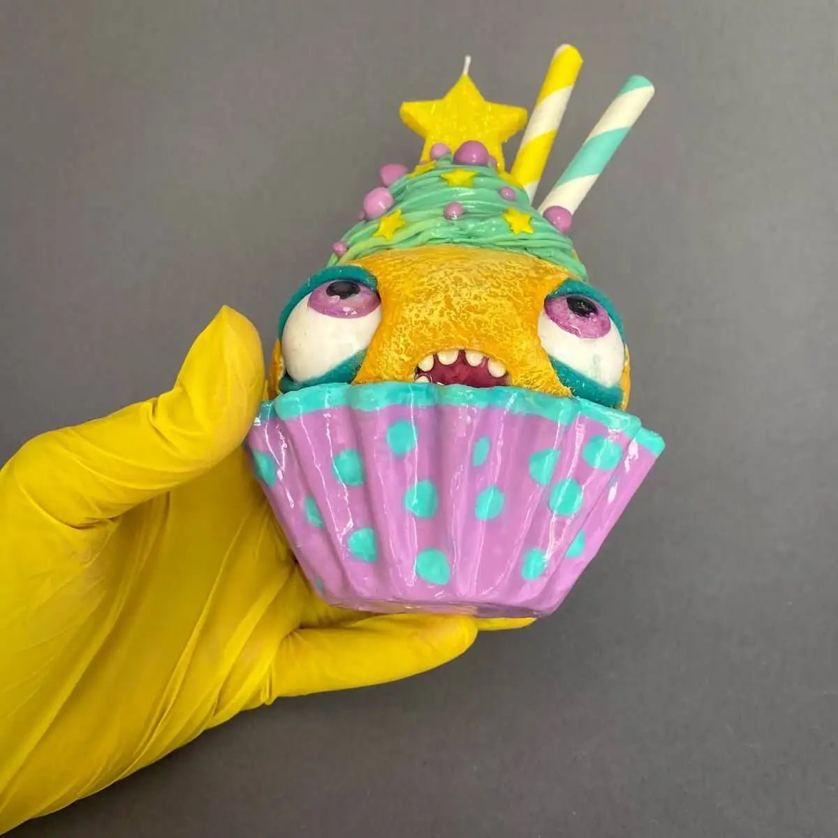 Handmade cupcake figurine held in yellow-gloved hands
