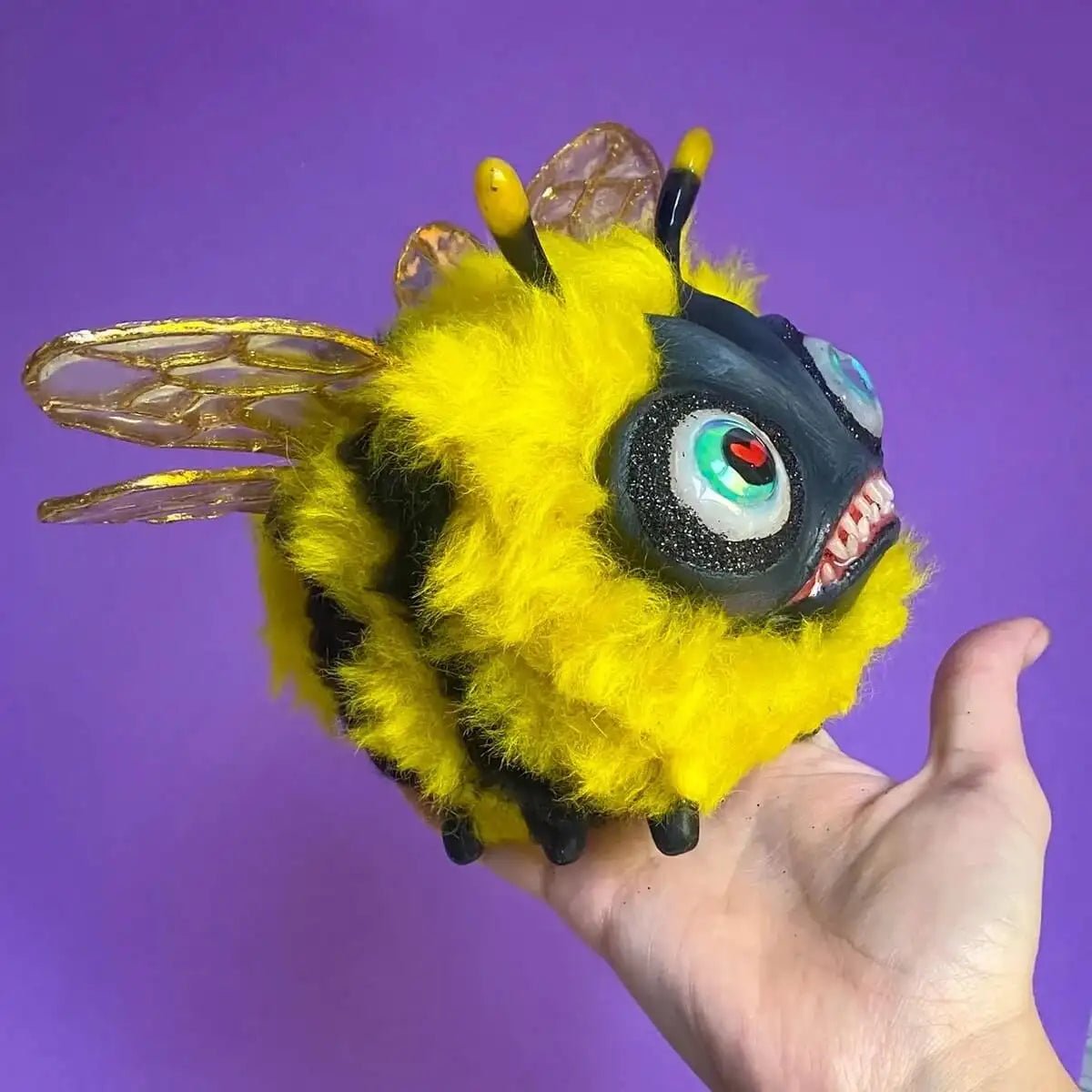 Papier-mâché fluffy bee sculpture shown in hand for scale