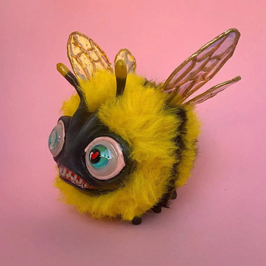 Papier-mâché fluffy bee figurine on pink background with wide eyes and fuzzy texture