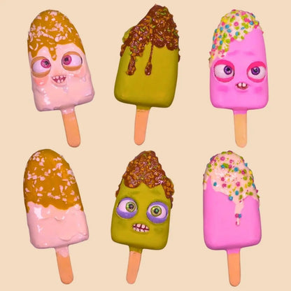 Collection of six colorful papier-mâché ice cream popsicles with cartoon faces and toppings