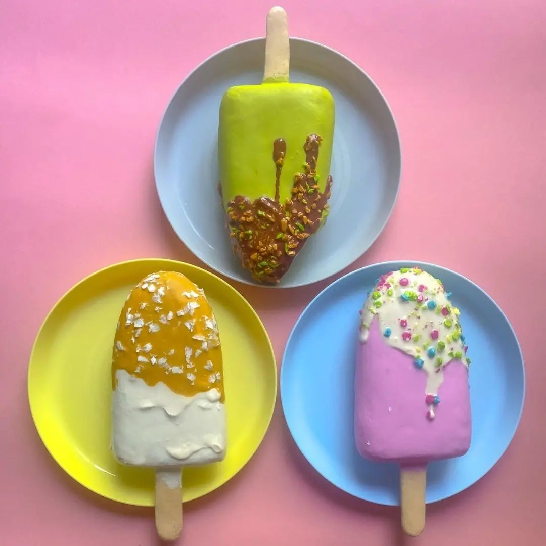 Set of three colorful papier-mâché ice cream popsicles with caramel, sprinkles and nuts on plates