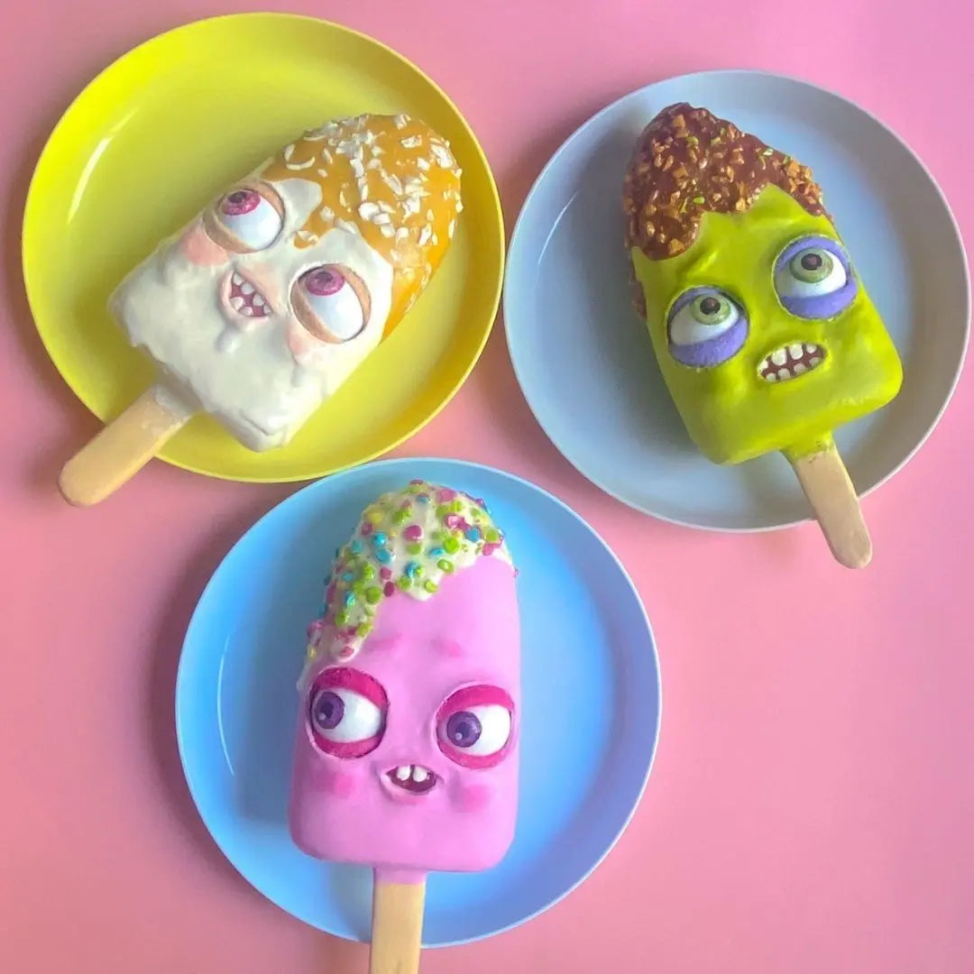 Set of three papier-mâché ice cream popsicles with funny cartoon faces on colorful plates
